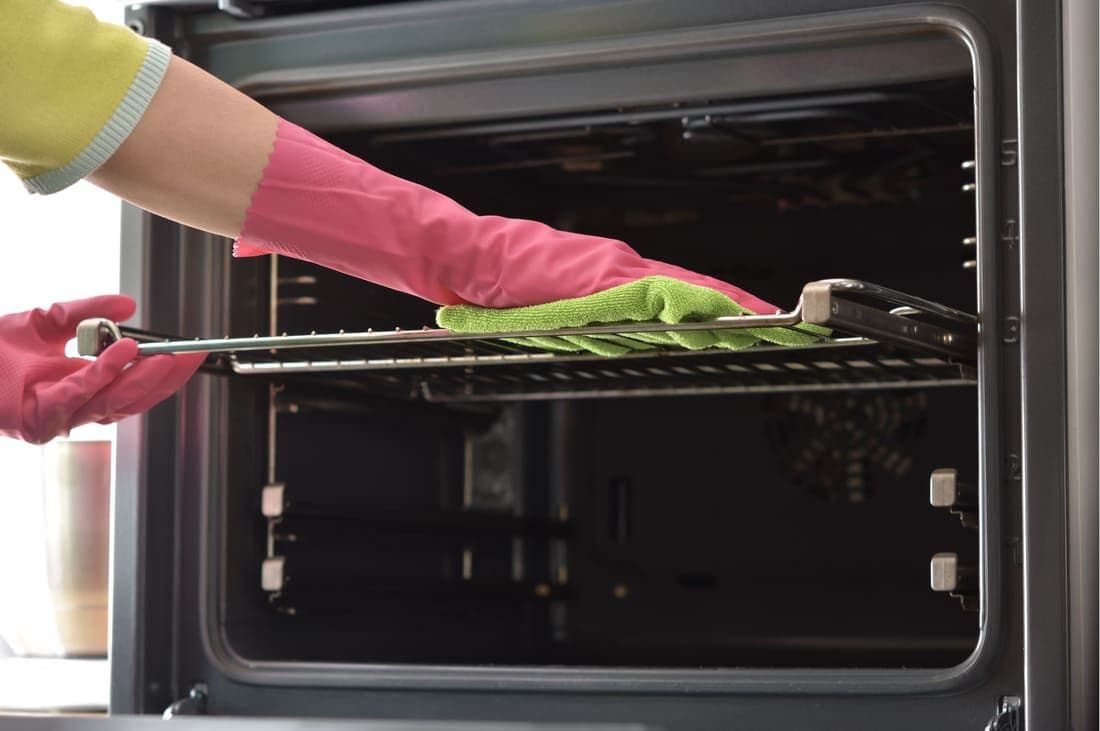 Close-up of a cleaner degreasing an oven rack and door during a professional oven clean